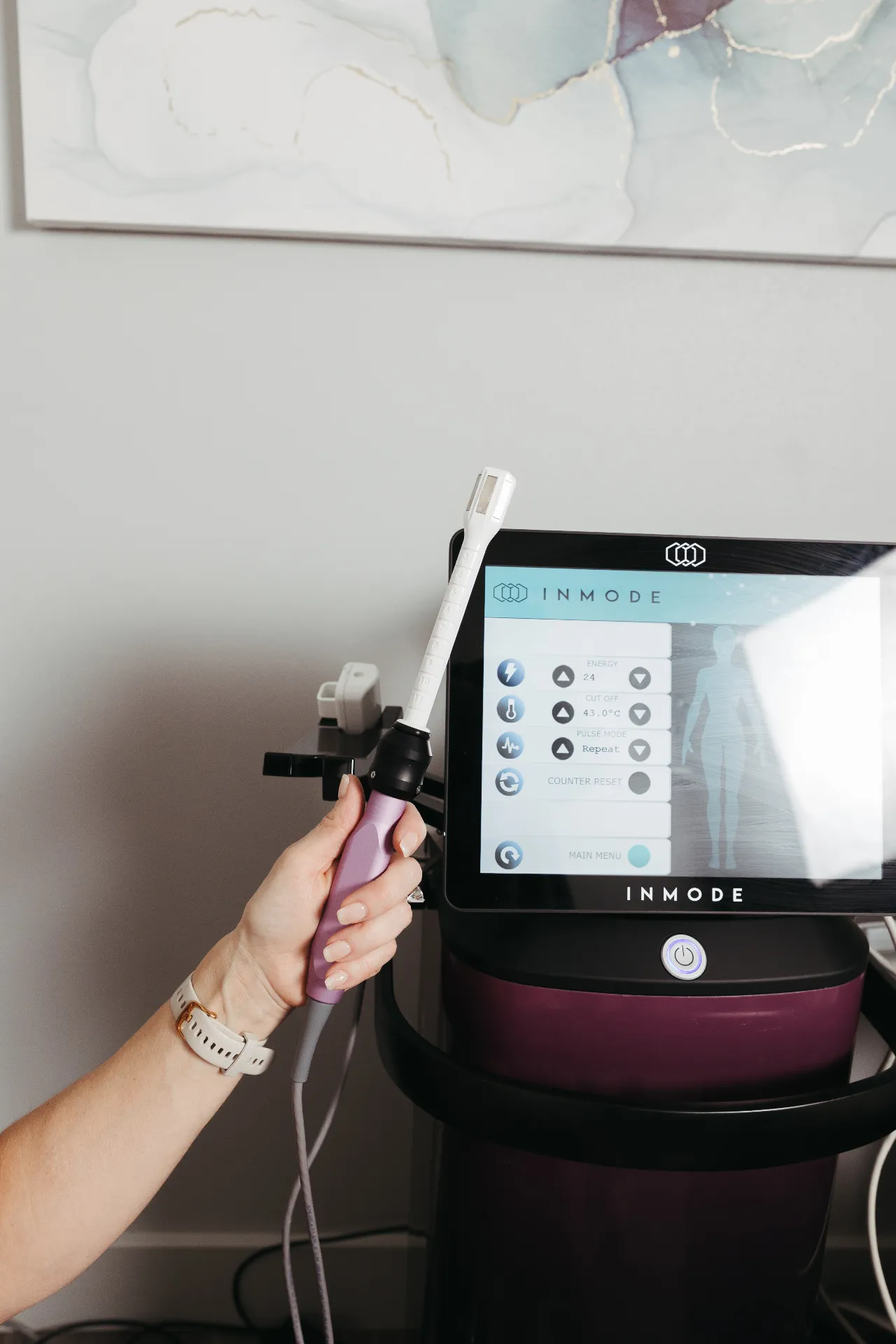 Hand holding a FormaV radiofrequency device in front of an InMode machine at Encompass Wellness