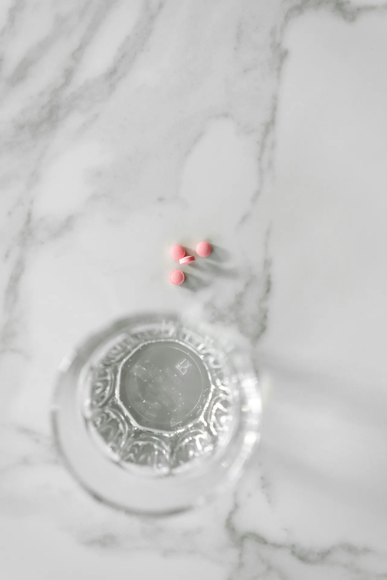 Pink Oral Hormone Replacement Therapy tablets beside a glass of water